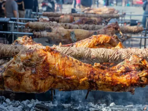Plusieurs agneaux à la broche rôtissent lentement sur des feux de bois. La peau dorée et croustillante promet un délice savoureux.