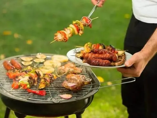 Un homme prépare un barbecue avec des brochettes et des saucisses. Qui a inventé le barbecue ? Mystère !