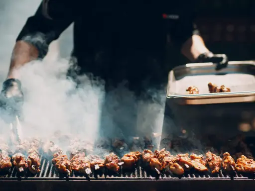 Un chef prépare un délicieux barbecue italien, des brochettes de viande fumantes sur le grill.