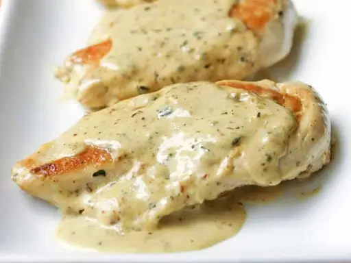 Deux morceaux de poulet à la crème, nappés d'une sauce onctueuse aux herbes, sur une assiette blanche. Un délice !
