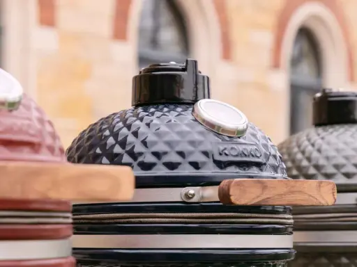 Trois barbecues kamado de couleurs différentes, prêts pour un avis. Le noir est au centre, le rouge à gauche, le gris à droite.