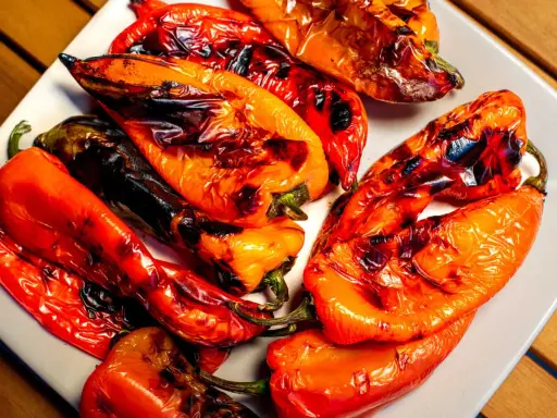 Poivrons rouges et orangés grillés au barbecue, légèrement noircis par la cuisson, sur une assiette blanche.