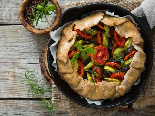 Tarte aux légumes colorée, garnie de tomates, courgettes et aubergines, prête à être dégustée.
