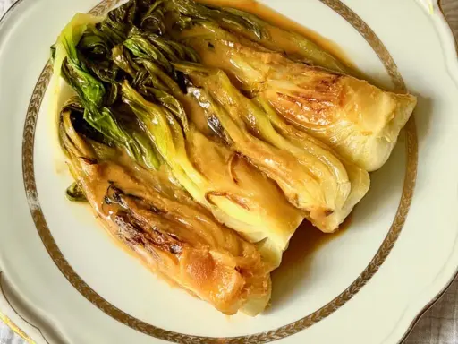 Pak choi braisé, tendre et savoureux, nappé d'une sauce dorée, servi sur une assiette élégante.
