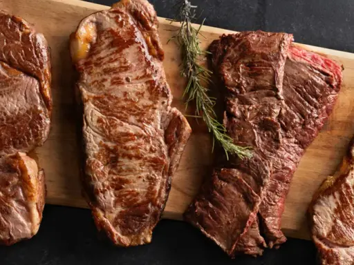 Quatre pièces de viande de saison octobre, grillées à la perfection, sur une planche en bois avec des herbes et du sel.