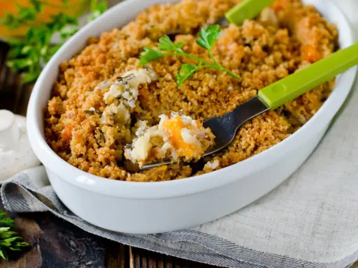 Un délicieux crumble salé aux légumes et riz, servi dans un plat blanc, avec une fourchette verte prête à déguster.