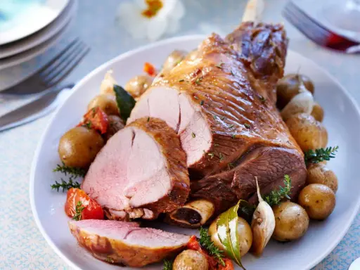 Un gigot d'agneau rôti, tranché, servi avec des pommes de terre nouvelles, tomates et ail. Parfait pour savoir que faire avec des morceaux de gigot d'agneau.
