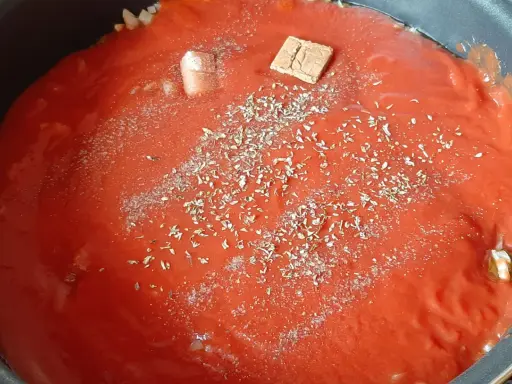 Sauce tomate maison mijote dans une poêle, agrémentée d'herbes et d'un cube de bouillon.