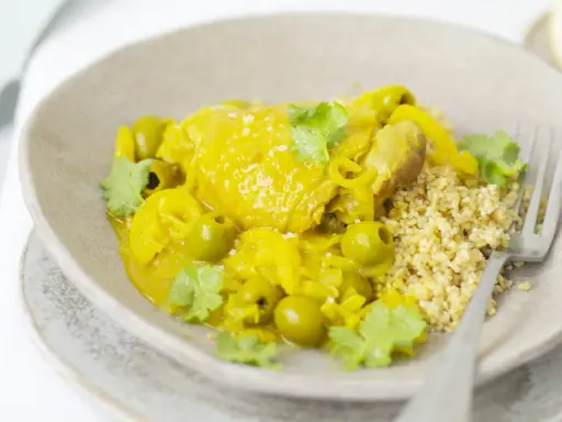 Un plat de tajine poulet citron, garni d'olives vertes et de coriandre fraîche, servi avec du couscous.