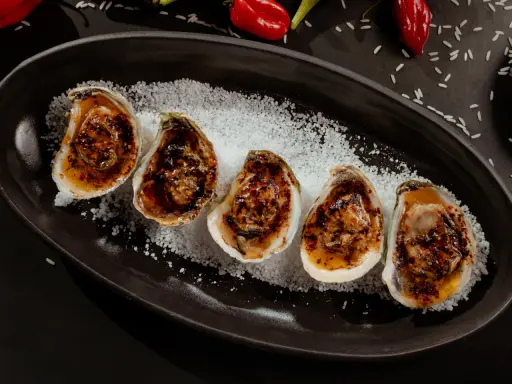 Cinq huîtres au barbecue, grillées et savoureuses, servies sur un lit de gros sel.