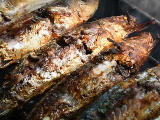 Plusieurs poissons entiers, dorés et appétissants, cuisent sur un barbecue au charbon. Quel poisson au barbecue charbon, une merveille !