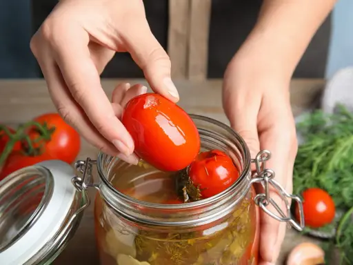 Mains ajoutant une tomate dans un bocal pour une recette de tomate farcie le parfait.
