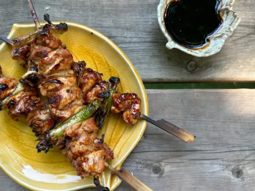 Brochettes yakitori savoureuses, laquées et grillées, servies sur une assiette jaune avec une sauce foncée à côté.