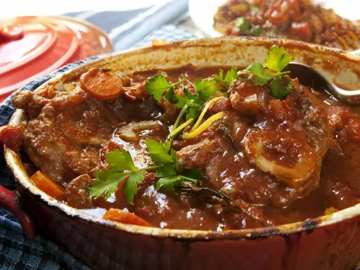 Un plat mijoté de veau marengo traditionnel, avec des morceaux de viande tendres dans une sauce tomate riche, garni de persil frais et de carottes.