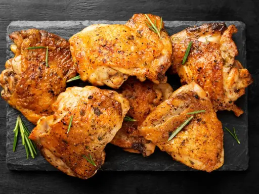 Pile de haut de cuisse de poulet grillé, assaisonné d'herbes et de poivre, sur une ardoise noire.