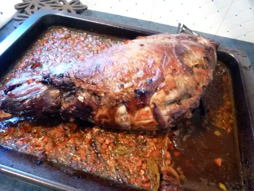Gigot de sanglier rôti 7h, baignant dans son jus avec des légumes coupés. Un plat savoureux prêt à être dégusté.