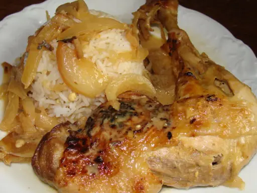 Un plat de poulet yassa savoureux avec du riz blanc et des oignons caramélisés.