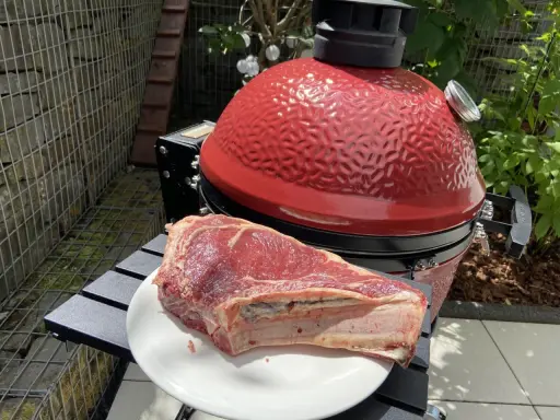 Une belle côte de bœuf crue attend sur une assiette blanche, prête à être grillée sur le barbecue rouge vif.