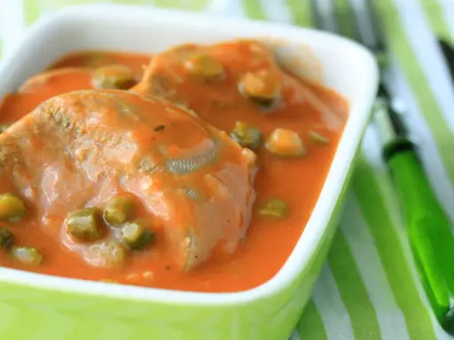 Tranches de langue de bœuf mijotées dans une sauce tomate onctueuse avec des petits pois. Un plat réconfortant servi dans un bol vert vif.