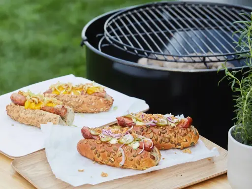 Délicieux hot dogs prêts pour un barbecue, avec des garnitures fraîches et un pain aux graines.