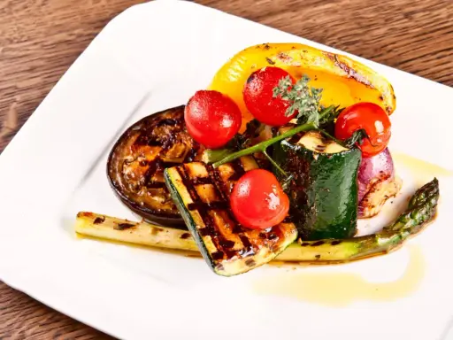 Légumes grillés : courgette, tomate, poivron jaune, aubergine, asperge et oignon rouge, arrosés d'une huile dorée.
