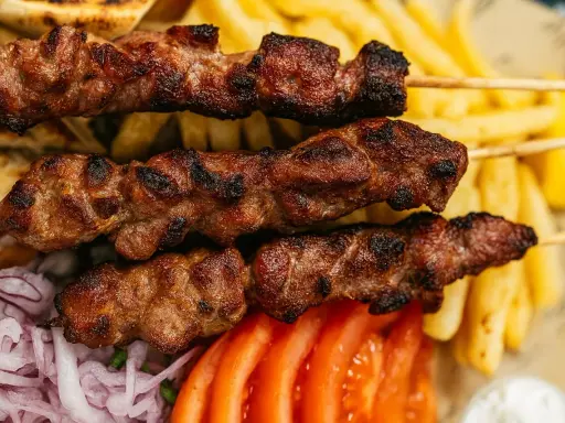 Brochettes de viande grillée, parfaites pour une cuisson indirecte au barbecue, accompagnées de frites, pain pita, tomates et oignons.