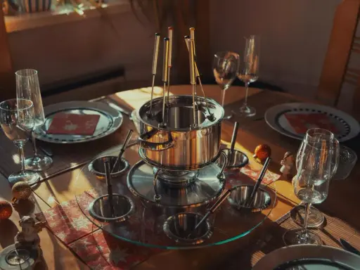 Service à fondue prêt pour un repas convivial. Le caquelon en inox est entouré de coupelles et de fourchettes, promettant une fondue sans huile savoureuse.