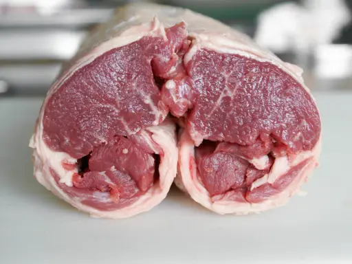 Un plat avec agneau cru, coupé en deux, révélant la chair rouge vif et le gras blanc. Prêt pour une cuisson savoureuse.