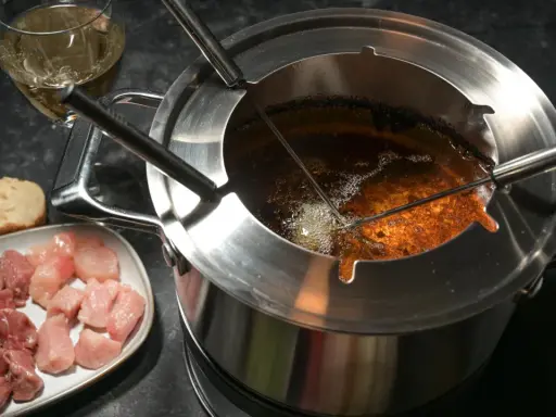 Préparation pour comment faire une fondue bourguignonne : morceaux de viande crue, pain et huile chaude dans le caquelon.
