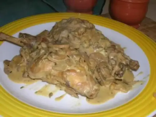 Un plat de lapin à la moutarde, crémeux et savoureux, servi sur une assiette blanche bordée de jaune.
