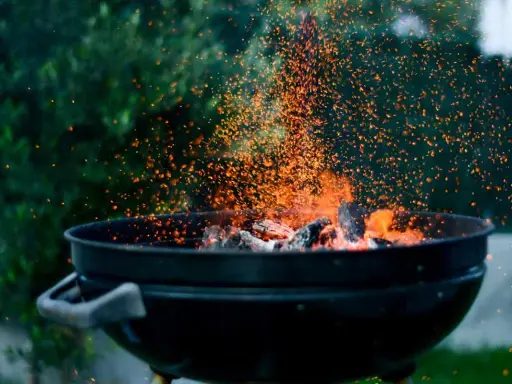 Un barbecue en plein air, avec des braises incandescentes et des étincelles qui dansent. L'odeur du barbecue bois ou charbon emplit l'air.