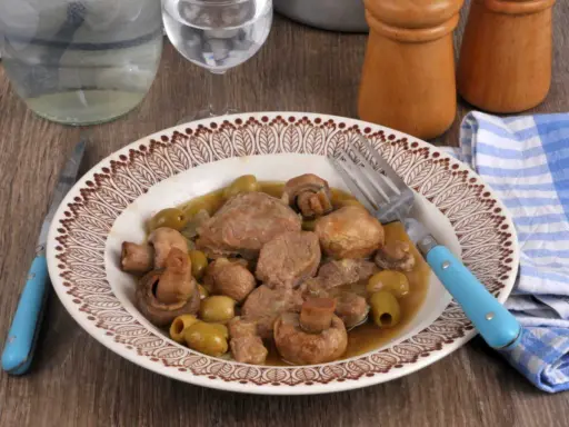 Un délicieux sauté de veau aux olives et champignons, servi dans une assiette décorée, prêt à être dégusté avec une fourchette bleue.