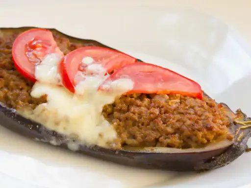 Aubergine farcie à la viande hachée, gratinée au fromage et garnie de rondelles de tomate. Une recette savoureuse et réconfortante.