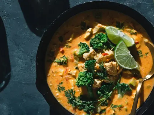 Un plat de poulet et brocolis baignant dans une sauce curry crémeuse, garni de quartiers de citron vert et de persil frais. Un délice !
