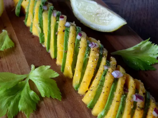 Une belle recette avocat et mangue, assaisonnée d'oignon rouge et de poivre, sur une planche en bois.