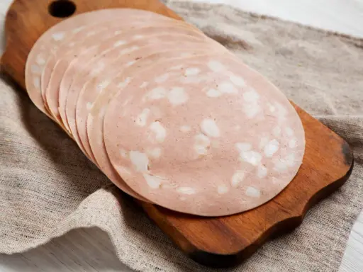 Tranches de mortadelle cuit ou cru, disposées en éventail sur une planche à découper en bois, sur un tissu de lin.