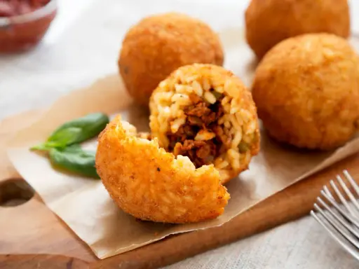Arancini dorés et croustillants, un délice de la recette arancini, servis avec du basilic frais.