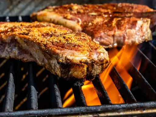 Deux entrecôtes savoureuses en cuisson sur un barbecue, les flammes dansent sous la viande.