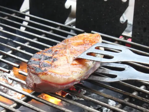 Magret de canard en cuisson indirecte sur un Weber, retourné avec une spatule. La peau est grillée et dorée, la chair rosée.