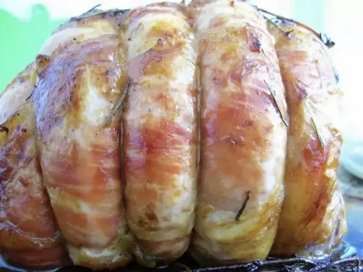 Un rôti de veau savoureux, enveloppé de lard et parsemé de romarin, prêt à être dégusté.