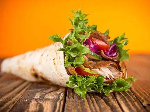 Un délicieux kebab maison garni de viande, salade croquante, tomates et chou rouge, sur un fond orange vif.