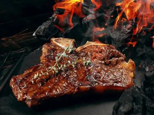Un steak T-bone juteux, garni de thym, cuit sur des braises ardentes. Une parfaite recette barbecue pour les amateurs de viande.