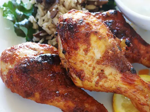 Trois pilons de poulet grillés et dorés, servis avec du riz et une tranche de citron.