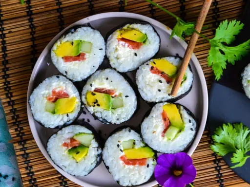Assiette de makis frais, parfaits pour une recette sushi maison. Avocat, saumon et concombre roulés dans du riz et des algues, parsemés de graines de sésame.