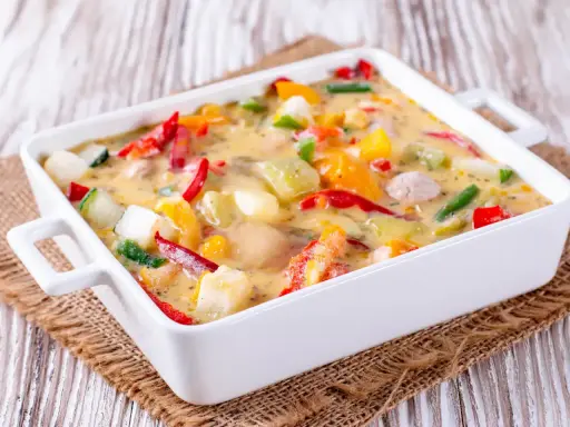 Un gratin de légumes coloré et crémeux, avec des poivrons, courgettes et autres légumes dans une sauce onctueuse, prêt à être dégusté.