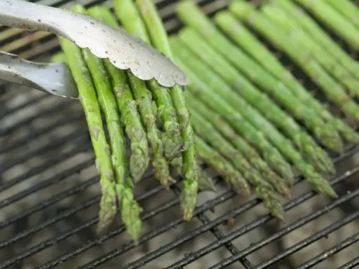 Des asperges vertes grillées, parfaites pour une recette simple et savoureuse. Les pinces saisissent un bouquet prêt à être retourné.