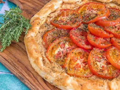 Une délicieuse tarte tomates aux herbes, sur une planche en bois, avec une branche de thym frais à côté.