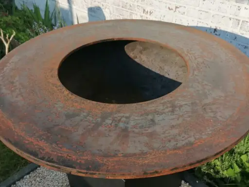 Gros plan sur le plateau rouillé d'un brasero, prêt pour son culottage. La surface métallique présente des nuances orangées et grises.