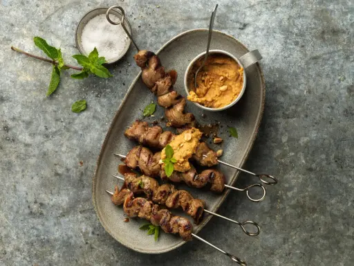 Brochettes d'agneau grillées au barbecue, servies avec une sauce aux arachides et garnies de menthe fraîche.