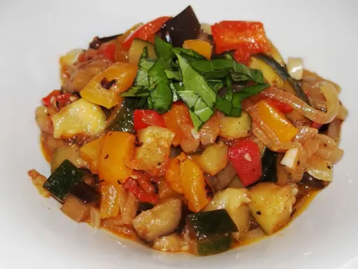 Un plat coloré de ratatouille recette, avec des dés de courgettes, aubergines, poivrons et tomates, garni de basilic frais.